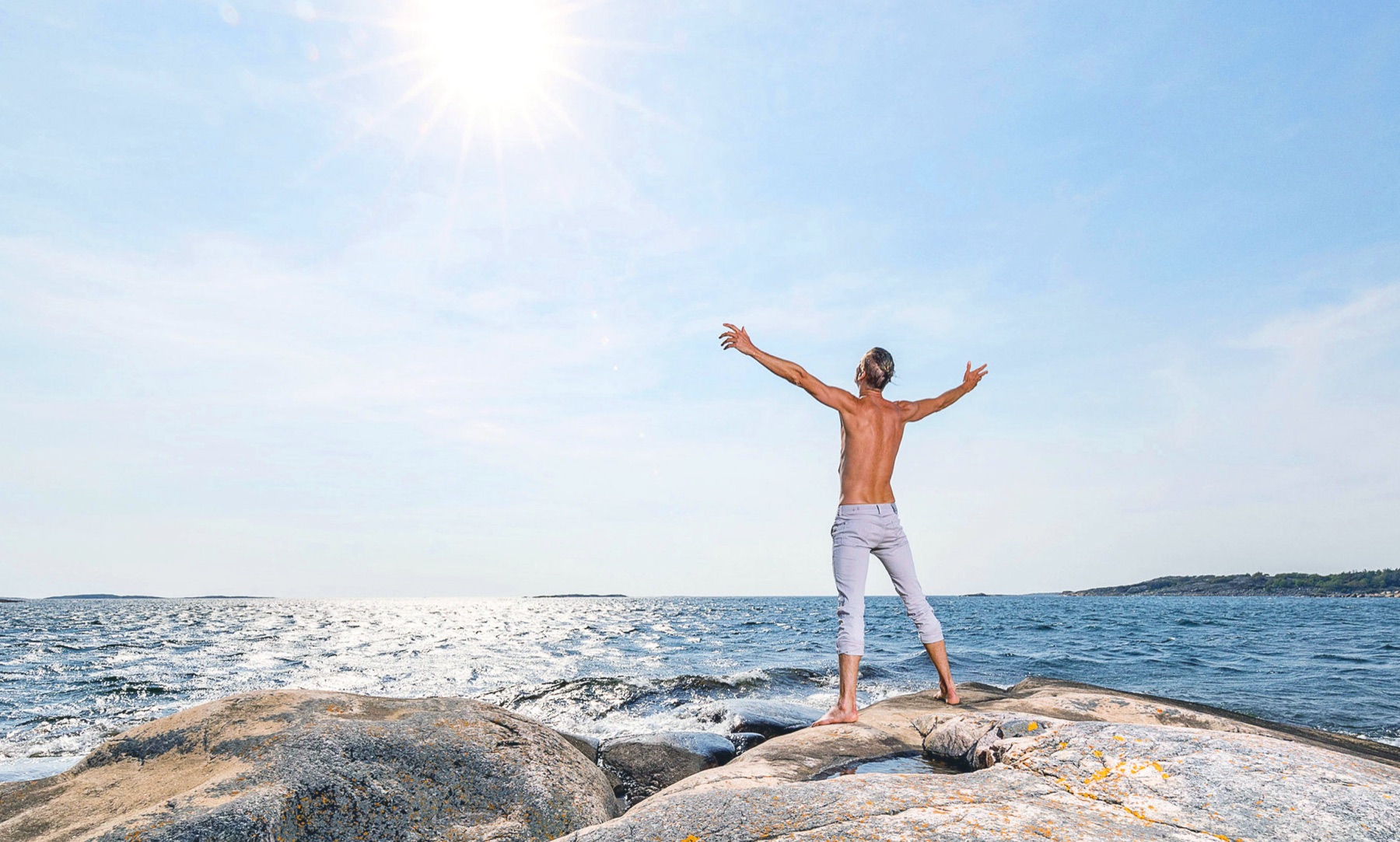 Niklas standing barefoot on coastal rocks with his arms open toward the sea