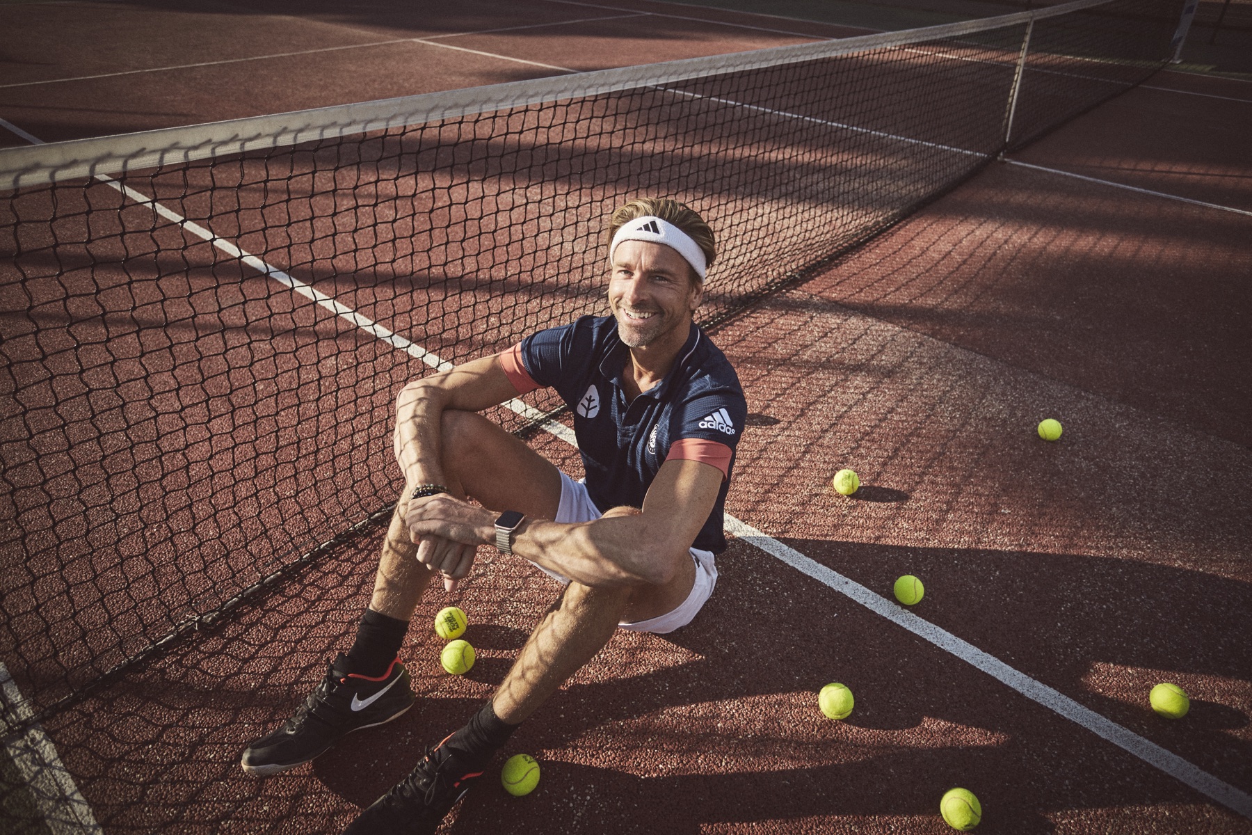 Niklas sitting beside a tennis net on a sunlit clay court